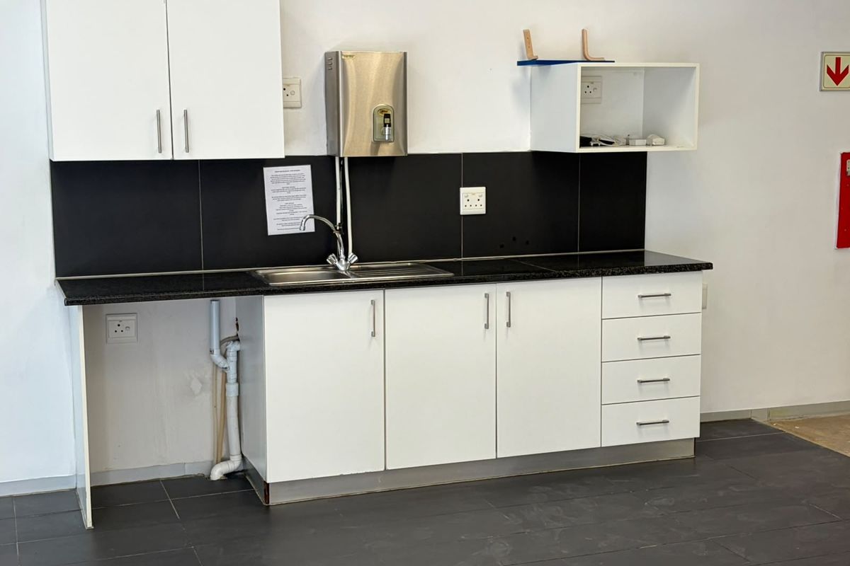 A functional office kitchenette featuring white cabinetry, a granite countertop, stainless steel sink, and a modern black tiled backsplash.