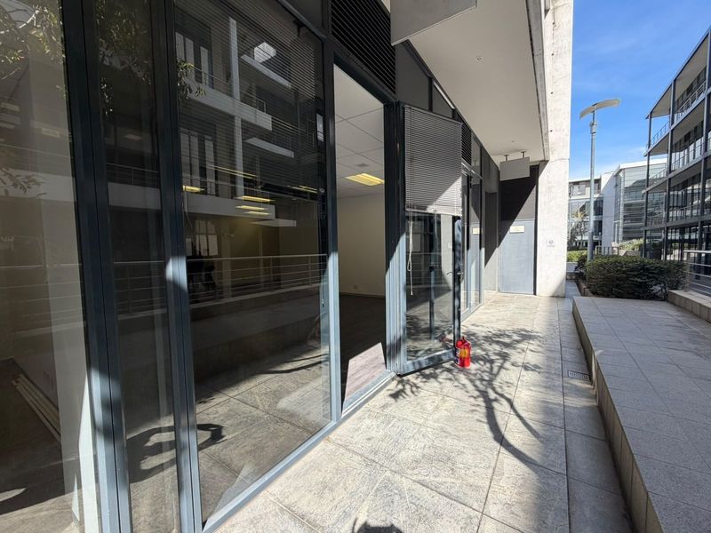 Modern office exterior featuring large glass sliding doors, a tiled patio area, and clean architectural lines in a professional business park setting.