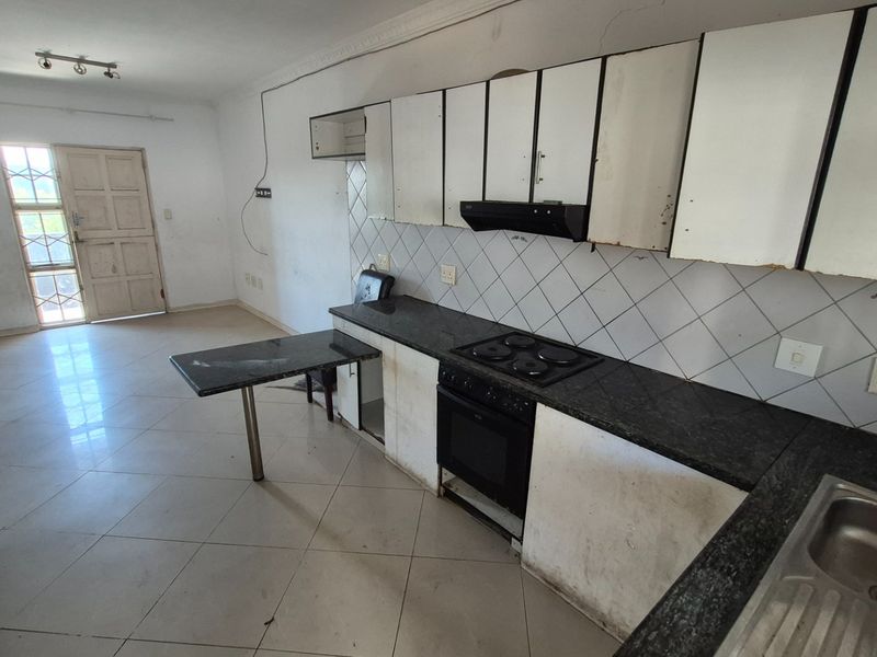 Open-plan kitchen and living area featuring granite countertops, built-in oven and hob, and tiled flooring. The space requires cosmetic updates and repairs.