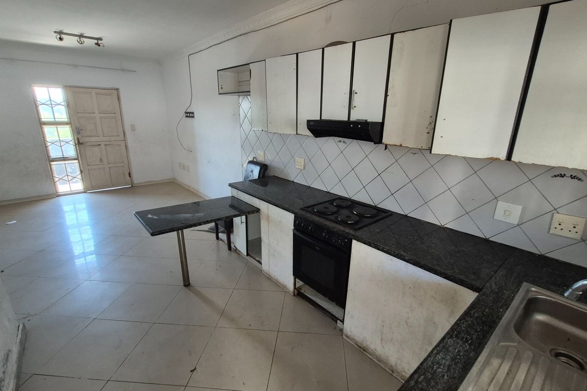 Open-plan kitchen and living area featuring granite countertops, built-in oven and hob, and tiled flooring. The space requires cosmetic updates and repairs.