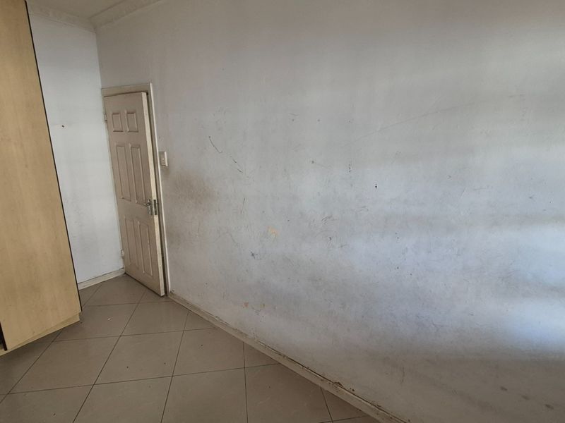 An empty bedroom featuring tiled flooring and a built-in wardrobe, currently requiring cosmetic attention to the wall surfaces.