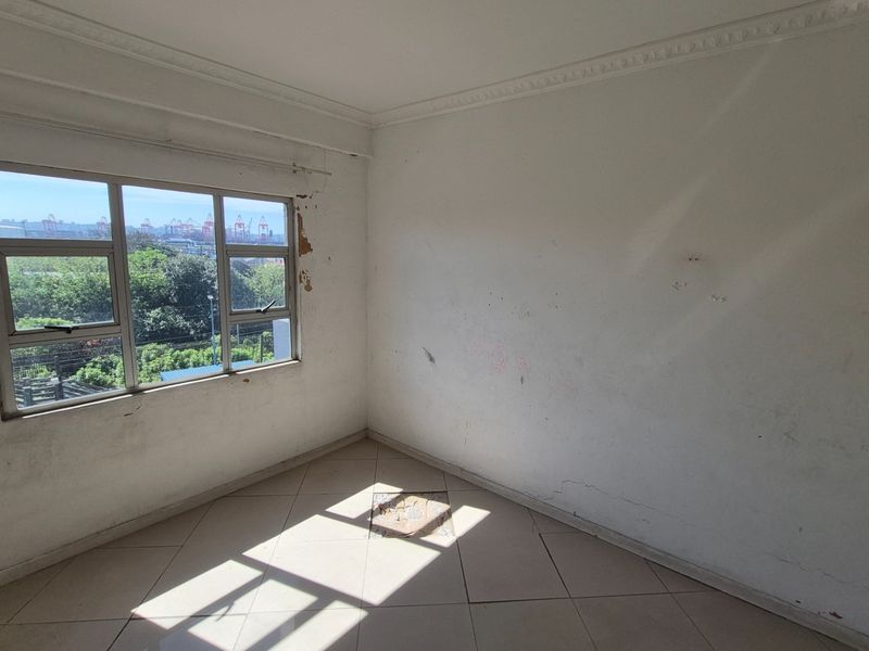 An empty bedroom featuring tiled flooring and an aluminium window frame, requiring cosmetic repairs to walls and flooring.