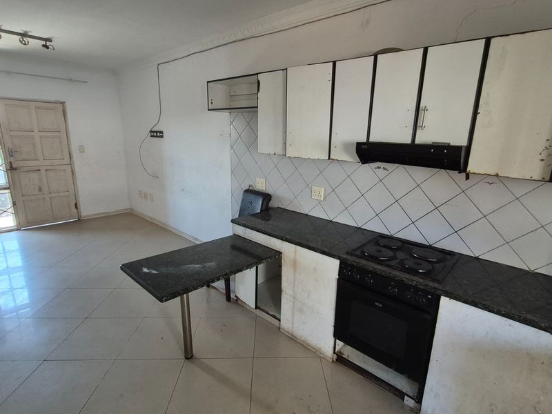 Open-plan kitchen and living area featuring granite countertops, built-in oven and hob, and tiled flooring, requiring cosmetic updates and repairs.