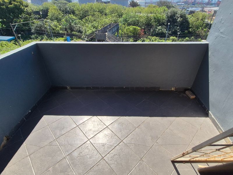 An open-air balcony featuring tiled flooring and solid masonry walls, offering an elevated view of the surrounding area.