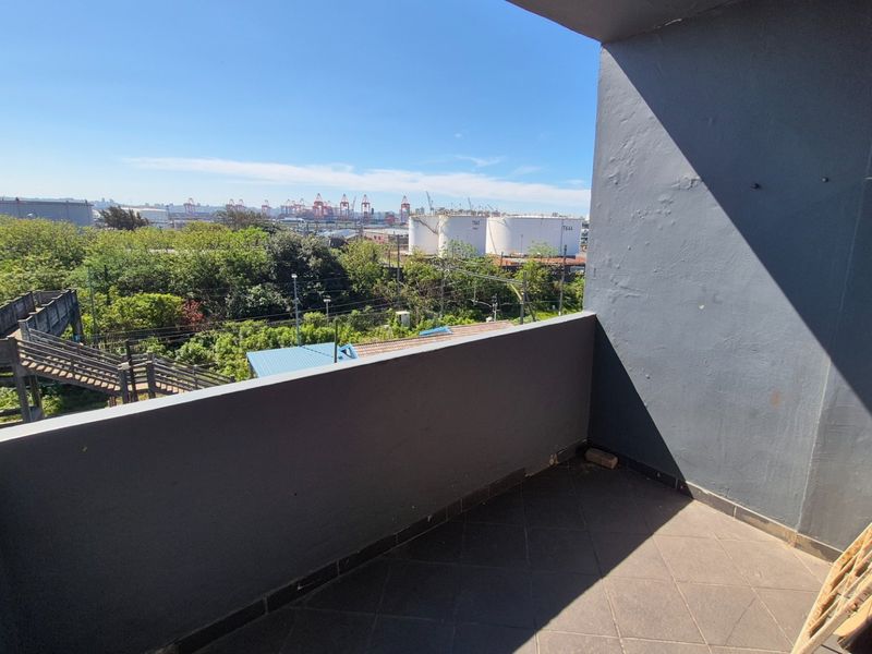 An open balcony featuring tiled flooring and a solid masonry balustrade, offering an elevated view of the surrounding industrial and green landscape.