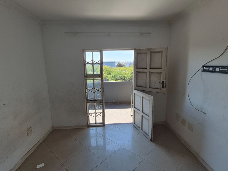 An empty bedroom featuring tiled flooring, coving, and direct access to a balcony through a security gate.