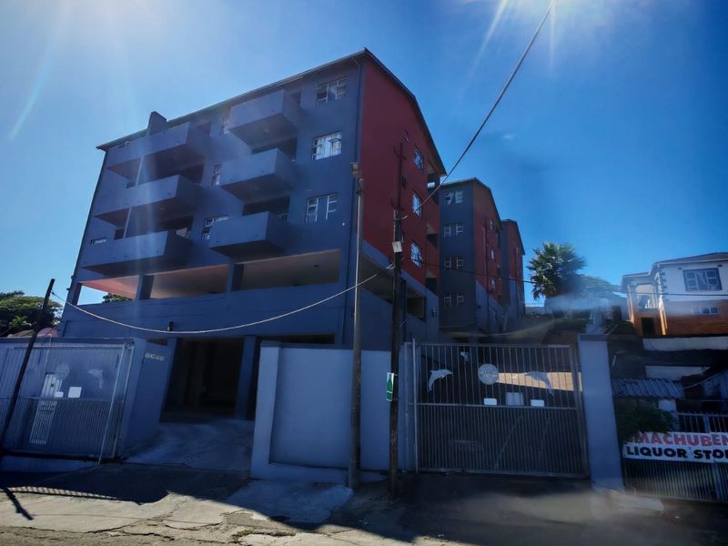 Exterior view of a multi-story apartment building featuring balconies, a secure gated entrance, and covered ground-level parking.
