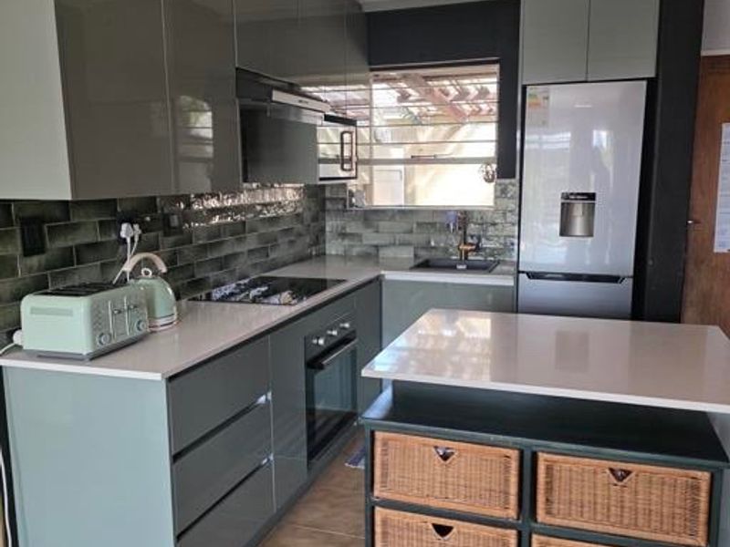 Modern kitchen featuring sleek grey cabinetry, stone countertops, subway tile backsplash, and a functional island with integrated storage.