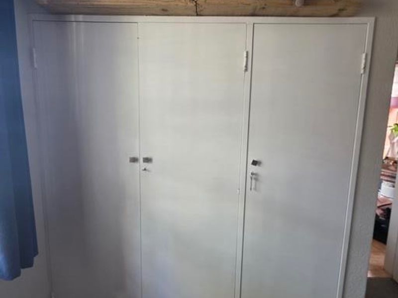 A bedroom featuring a white three-door built-in wardrobe with a wooden floating shelf mounted above.