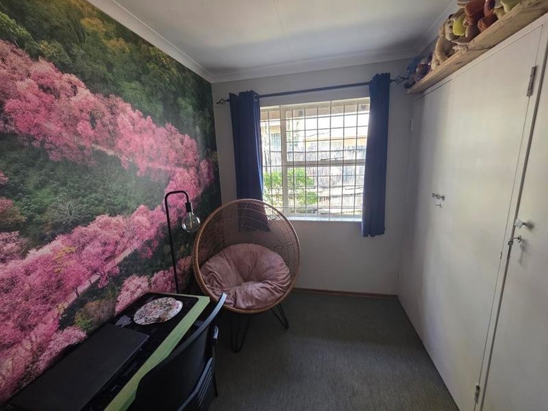 A compact bedroom featuring a built-in wardrobe, security bars on the window, and decorative wall covering.