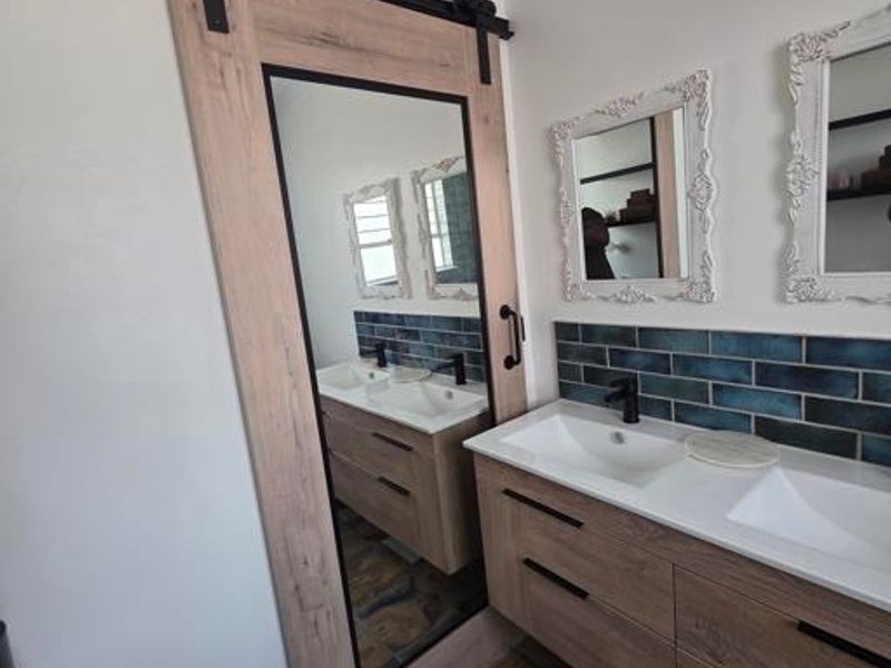 Modern bathroom featuring a double vanity with stone flooring, blue subway tile backsplash, and a stylish sliding barn door with an integrated mirror.