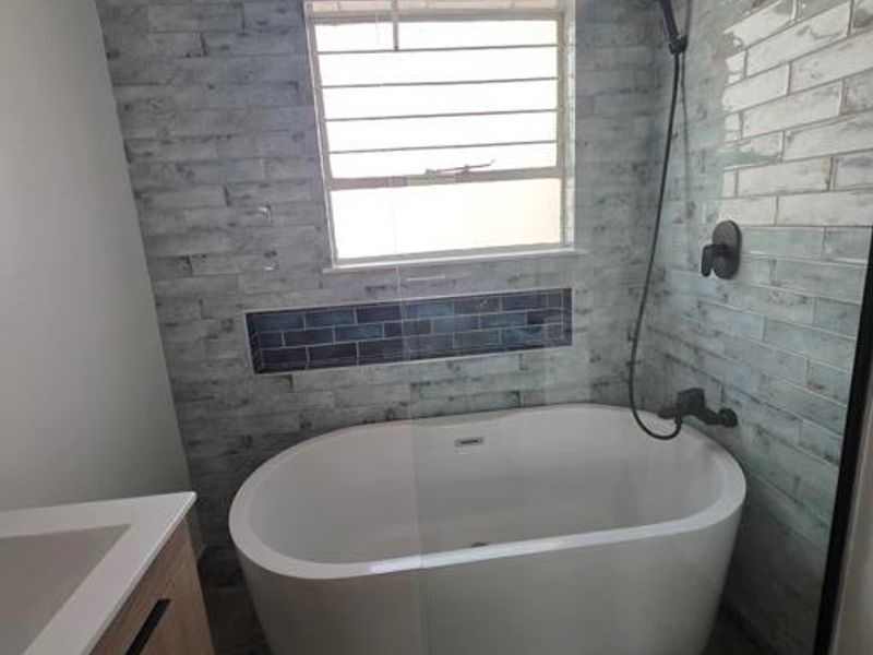 Modern bathroom featuring a freestanding bathtub, glass shower screen, rain shower head, and a contemporary vanity cabinet with stylish wall tiling.