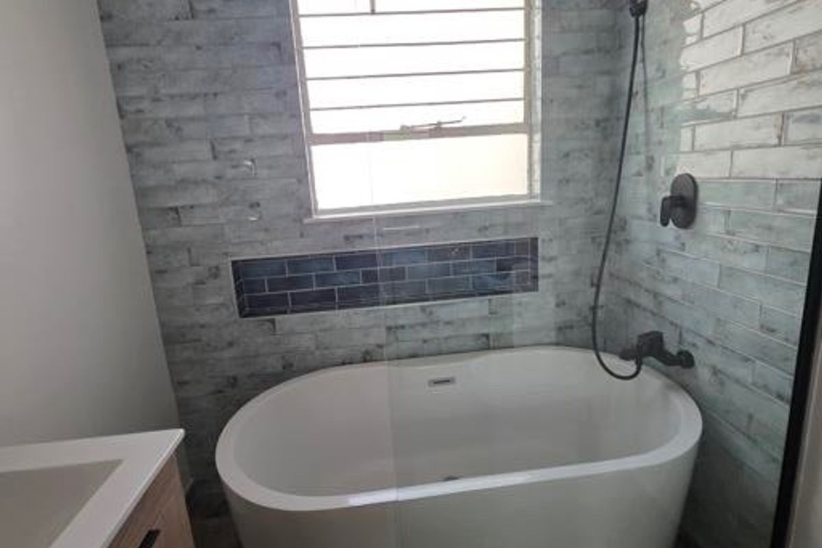 Modern bathroom featuring a freestanding bathtub, glass shower screen, rain shower head, and a contemporary vanity cabinet with stylish wall tiling.