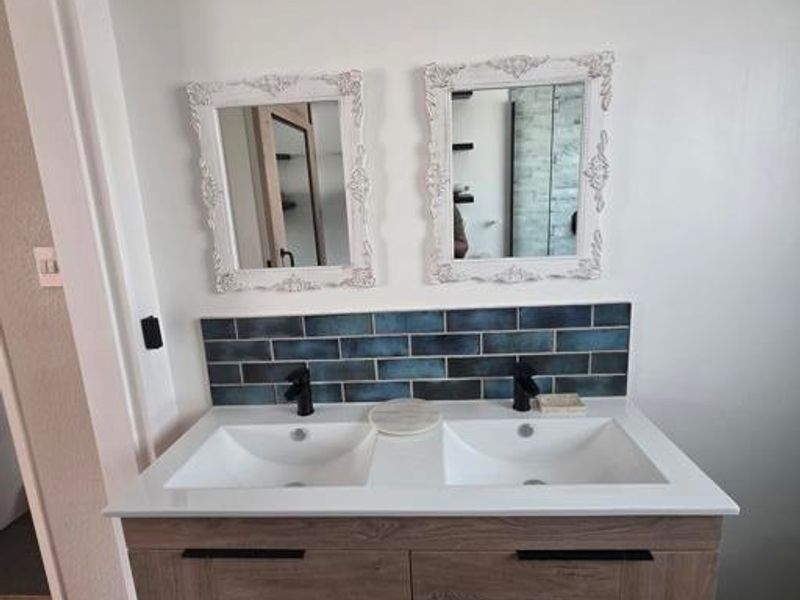 Modern bathroom vanity featuring a double sink setup, contemporary wood-finish cabinetry, black fixtures, and a stylish blue subway tile splashback.