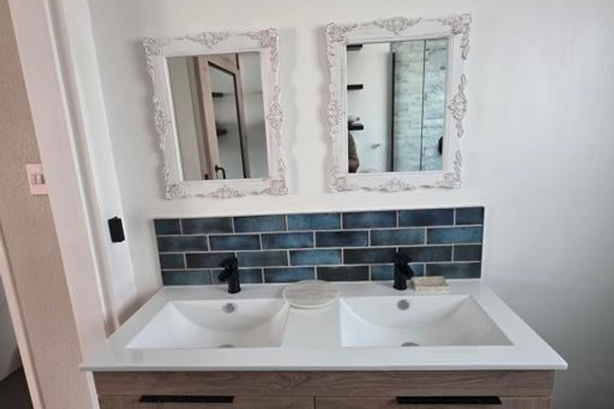 Modern bathroom vanity featuring a double sink setup, contemporary wood-finish cabinetry, black fixtures, and a stylish blue subway tile splashback.