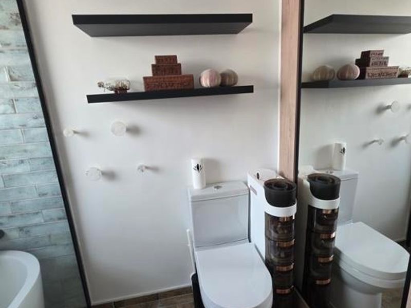 Modern bathroom featuring a white toilet, floating wall shelves, a large sliding mirror door, and decorative tiled flooring.