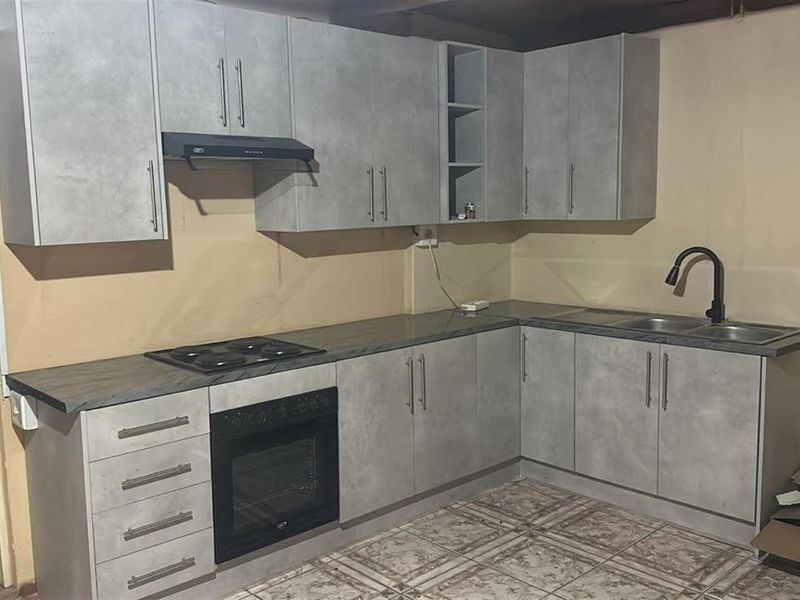 A functional kitchen featuring grey cabinetry, built-in oven and hob, and a double sink, currently requiring finishing touches to the wall surfaces.