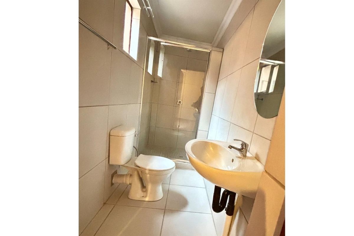 A functional bathroom featuring a shower enclosure, toilet, and wall-mounted basin with tiled finishes throughout.