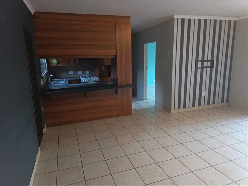 Open plan living area featuring tiled flooring and a compact kitchen with built-in cabinetry and a stove.