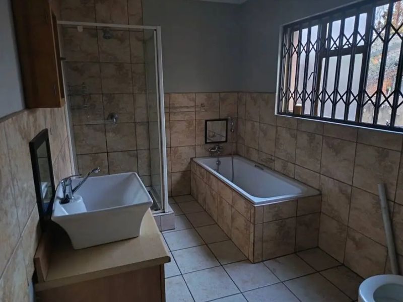 A functional bathroom featuring a tiled shower enclosure, built-in bathtub, vessel sink vanity, and a window with a security gate.