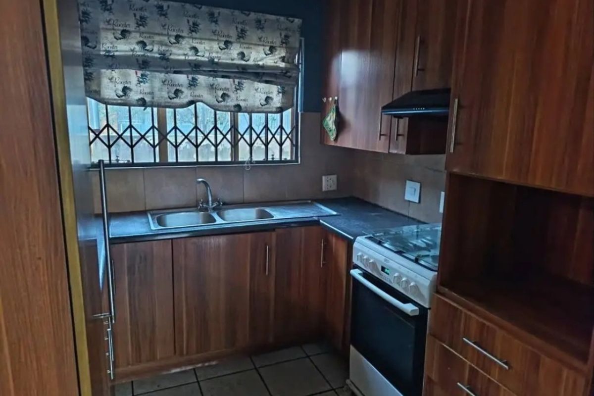 A functional kitchen featuring wood-look laminate cabinetry, a double bowl sink, a freestanding stove with extractor fan, and tiled flooring.