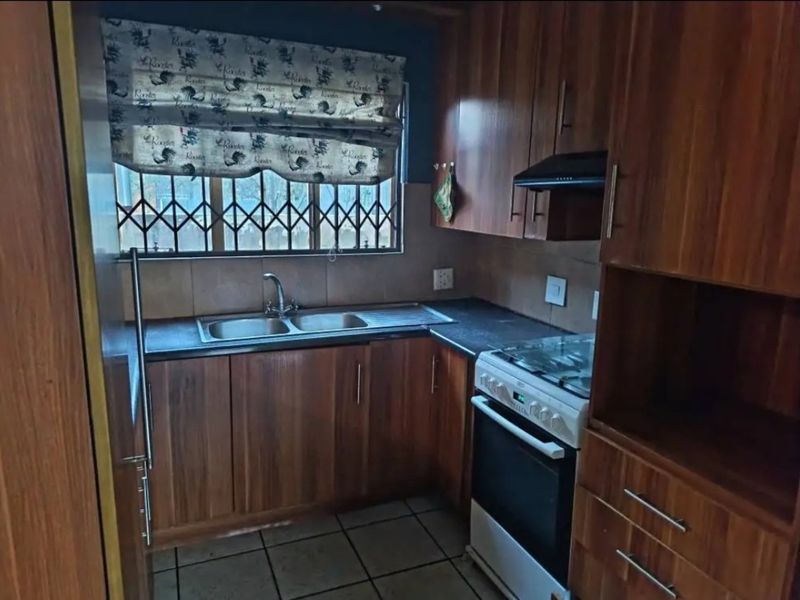 A functional kitchen featuring wood-look laminate cabinetry, a double bowl sink, a freestanding stove with extractor fan, and tiled flooring.