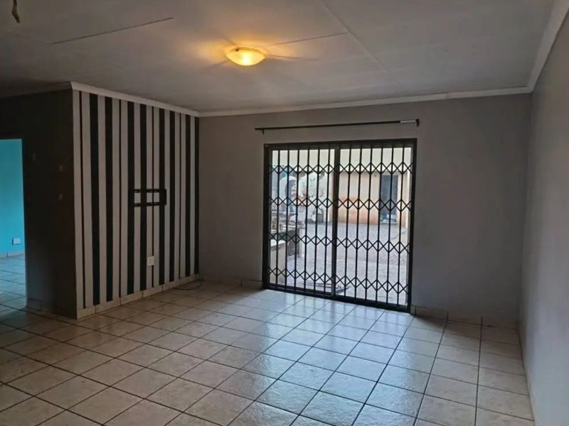 An empty living room featuring tiled flooring, a sliding glass door with a security gate, and a feature wall with striped wallpaper.