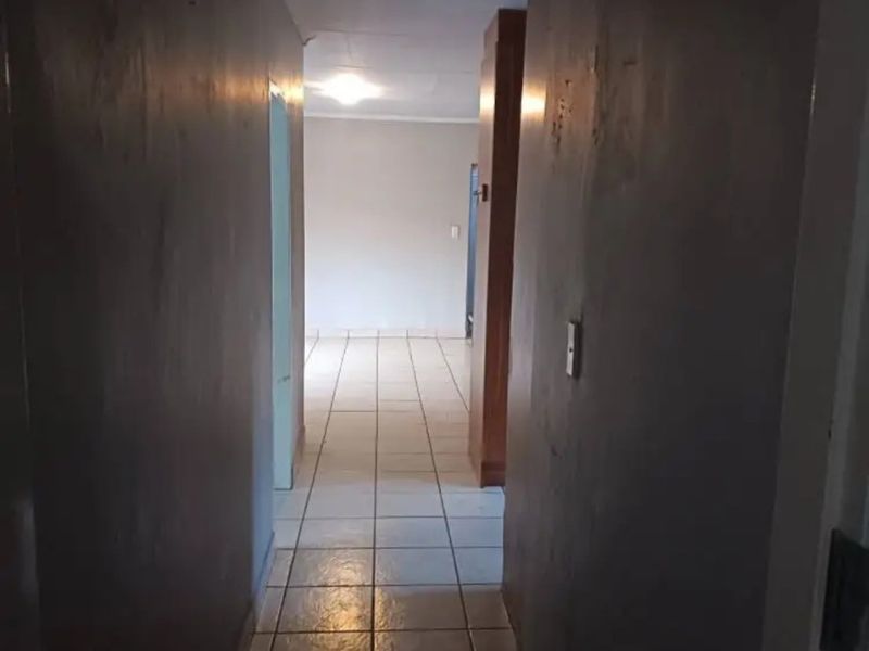 A narrow hallway featuring tiled flooring and built-in cabinetry, leading into an open living space.