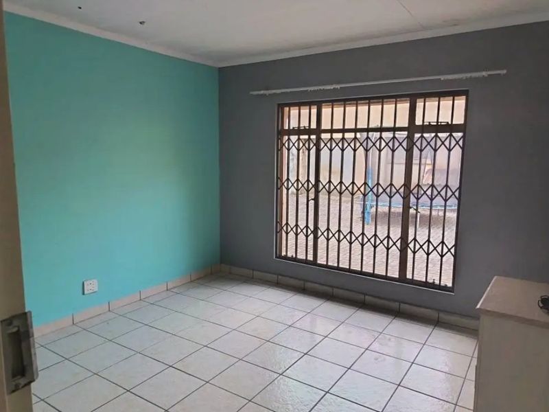 An empty bedroom featuring tiled flooring, security bars on the window, and dual-tone painted walls.