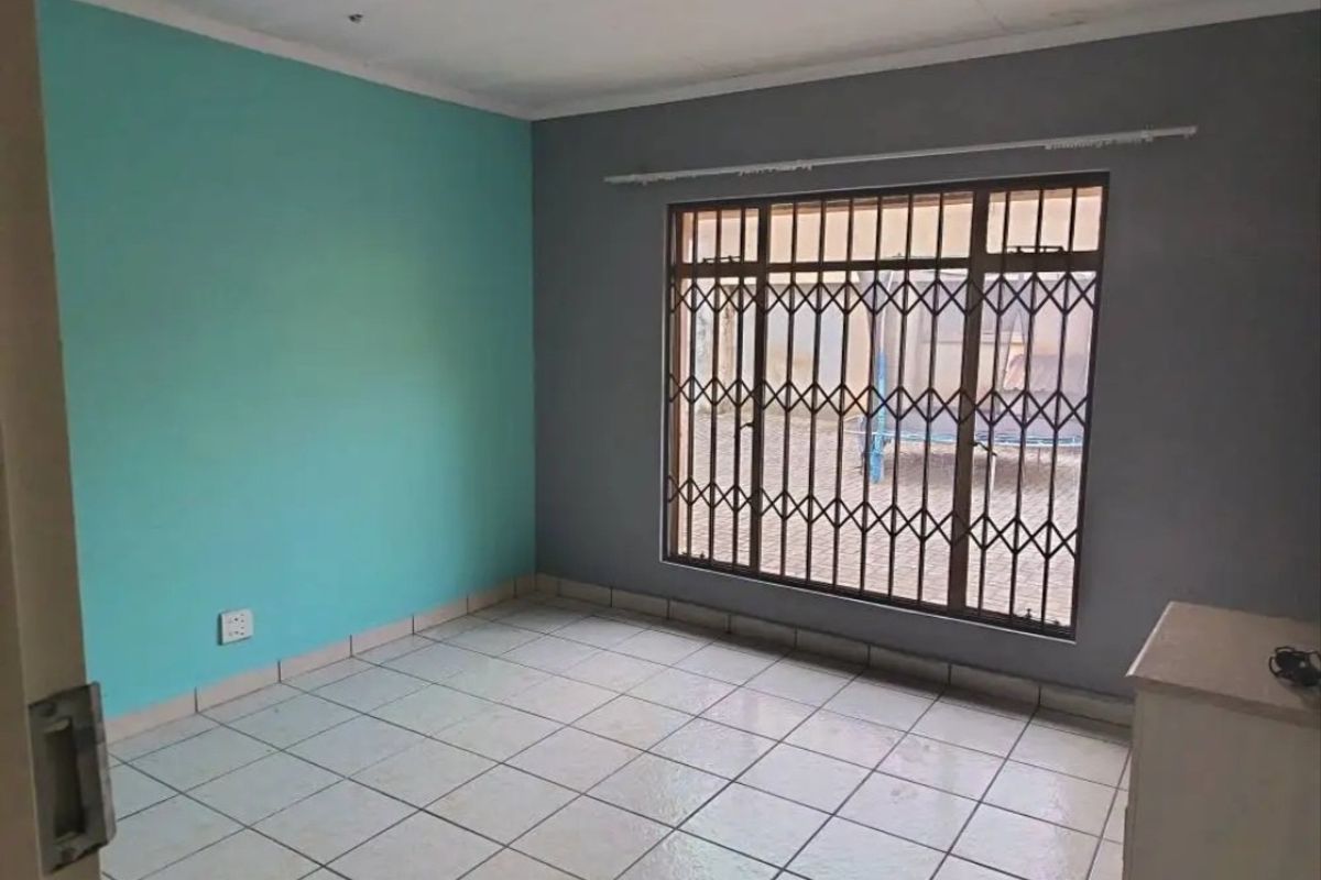 An empty bedroom featuring tiled flooring, security bars on the window, and dual-tone painted walls.