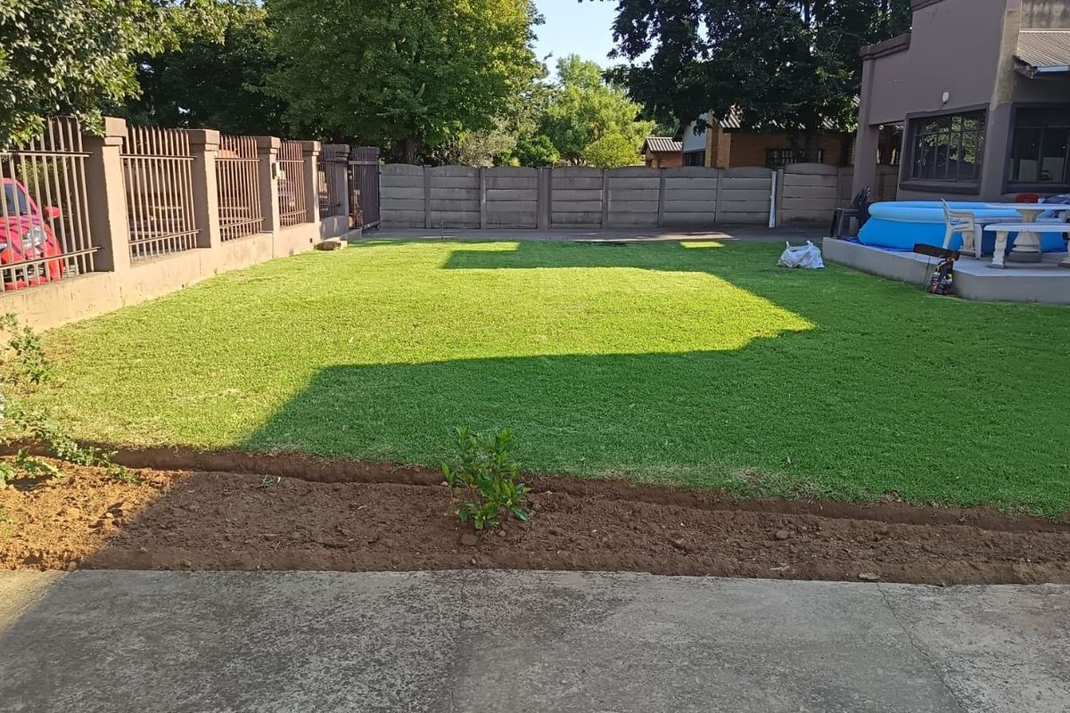 A spacious rear garden featuring a well-maintained lawn, concrete boundary walls, metal fencing, and a paved patio area.
