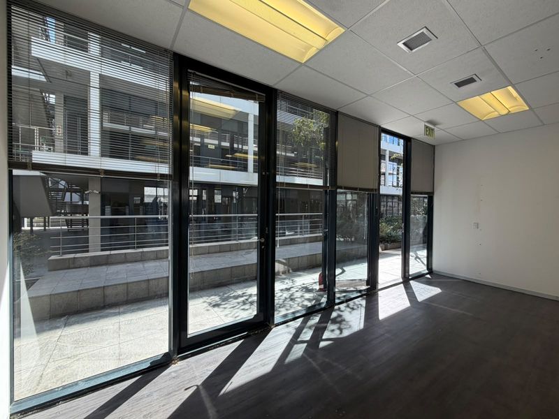 A bright, empty office space featuring large glass windows, laminate flooring, and a suspended ceiling with recessed lighting.