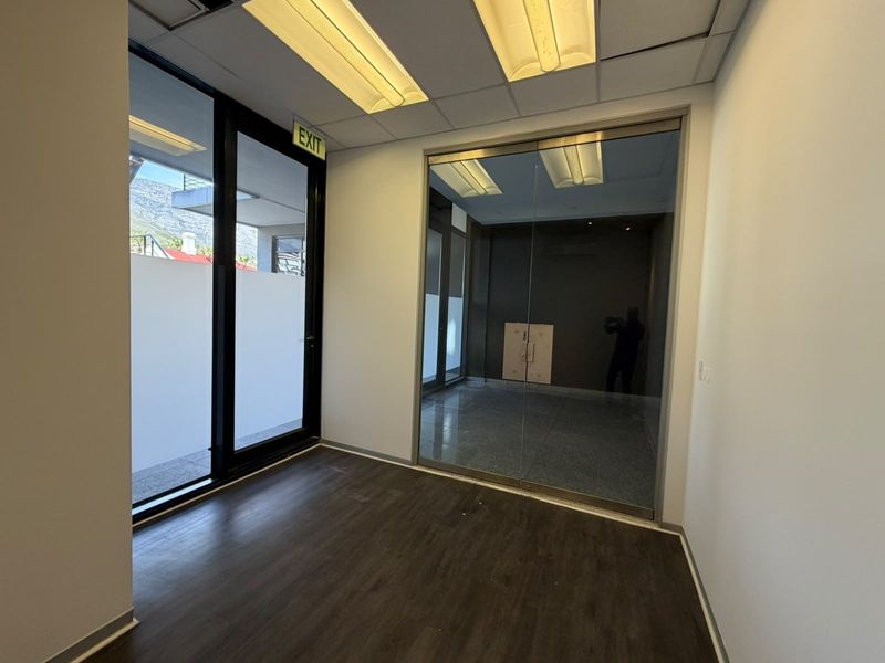 A modern, empty office space featuring a glass partition, laminate flooring, and recessed ceiling lighting, offering a clean and professional environment.