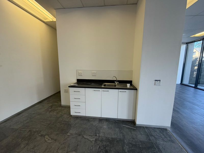 A compact office kitchenette featuring white built-in cabinetry, a dark stone countertop, a stainless steel sink, and modern tiled flooring.