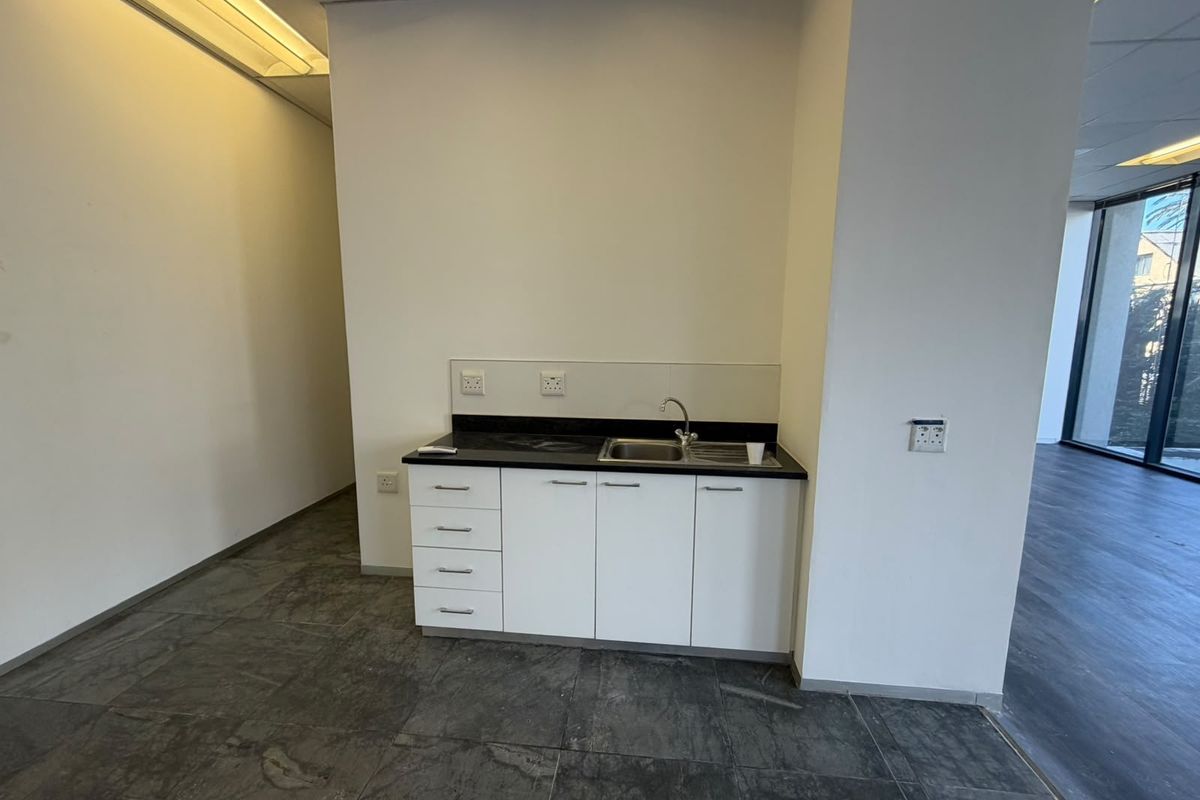 A compact office kitchenette featuring white built-in cabinetry, a dark stone countertop, a stainless steel sink, and modern tiled flooring.