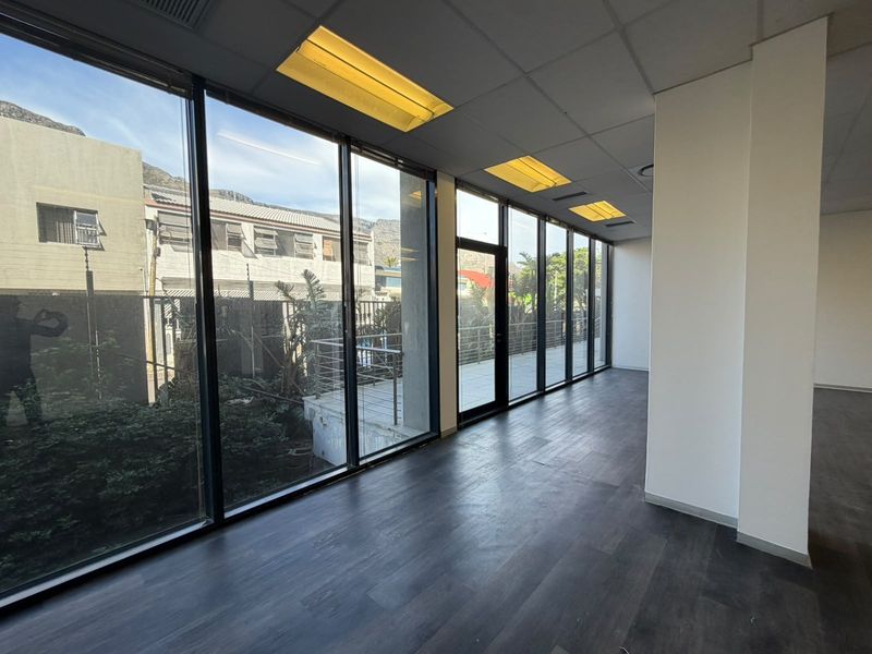 A bright, empty office space featuring floor-to-ceiling windows, dark laminate flooring, and recessed lighting, offering a clean and professional environment.