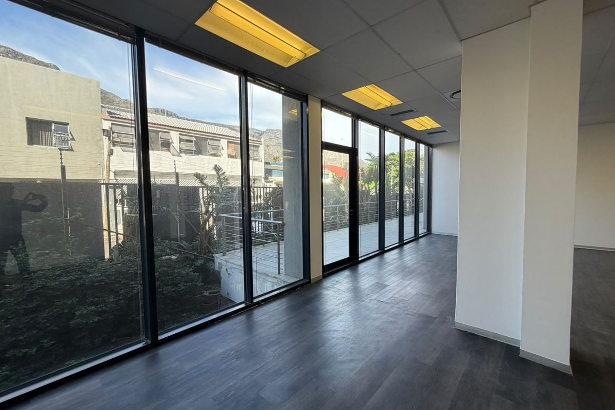 A bright, empty office space featuring floor-to-ceiling windows, dark laminate flooring, and recessed lighting, offering a clean and professional environment.