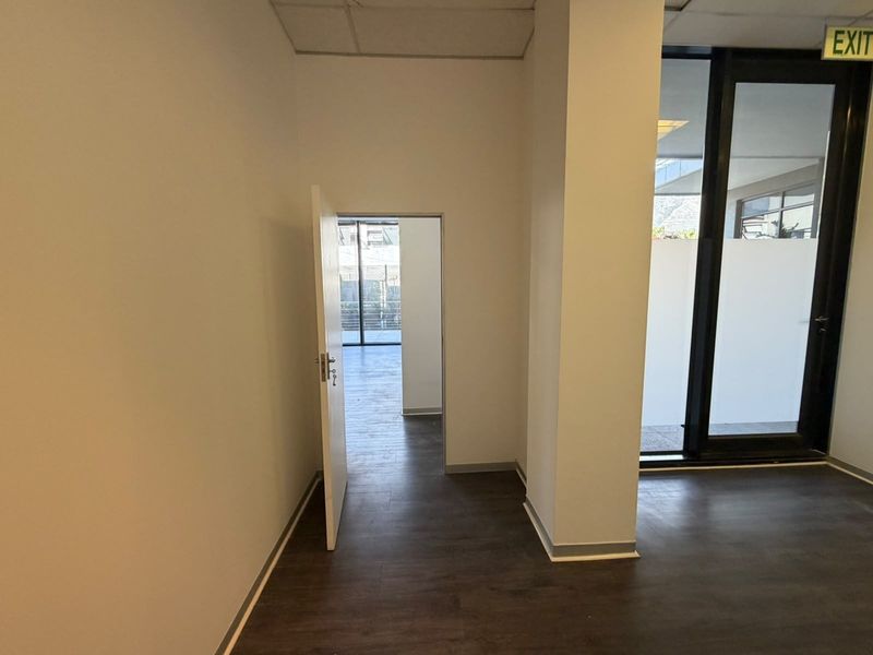 An empty office space featuring modern laminate flooring, a suspended ceiling, and a glass sliding door leading to an adjacent area.