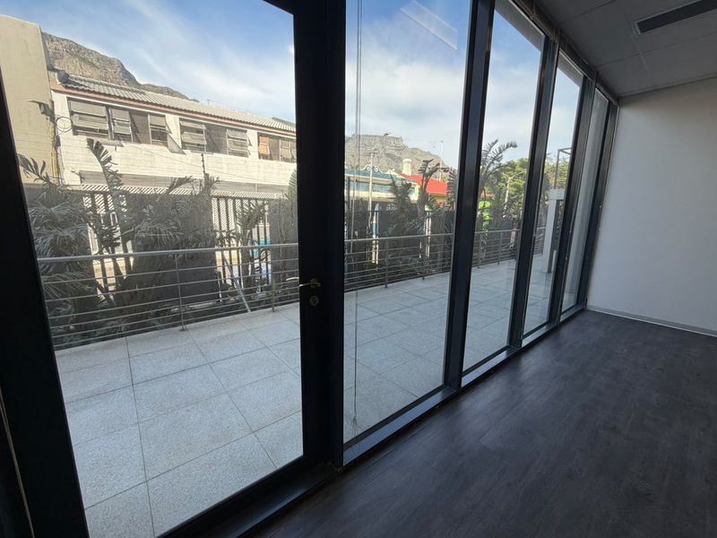 Empty office space featuring floor-to-ceiling windows and direct access to a private tiled balcony with mountain views.
