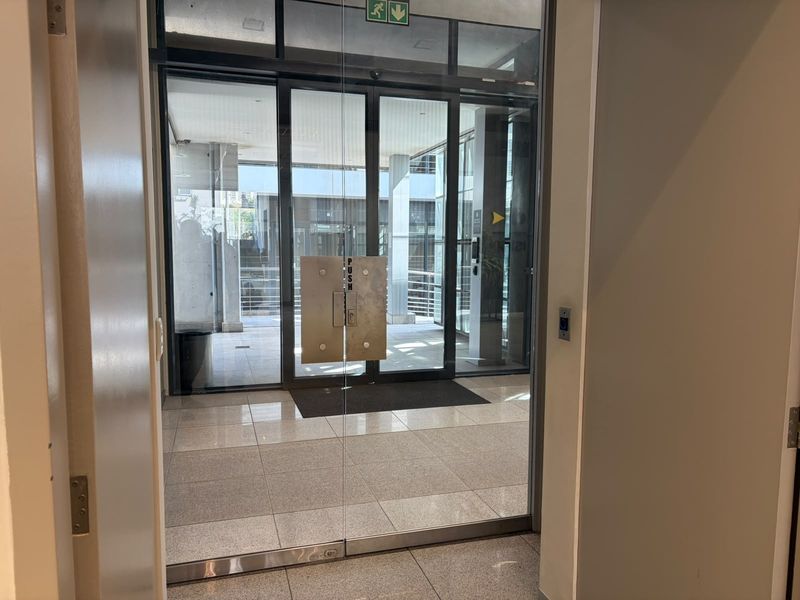 A clean and modern office building entrance featuring glass double doors and polished tile flooring, providing a professional and welcoming access point.
