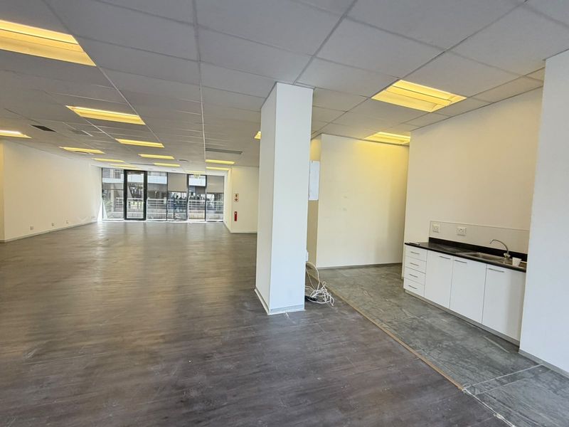 Spacious open-plan office area featuring a kitchenette, suspended ceilings with recessed lighting, and a mix of laminate and tiled flooring.