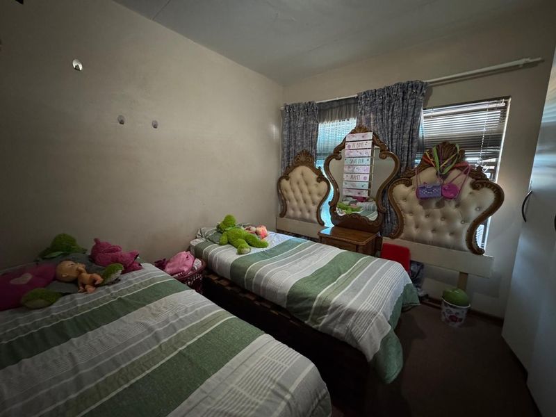 A bedroom featuring a window with curtain rails and carpeted flooring, requiring cosmetic updates to the walls and ceiling.