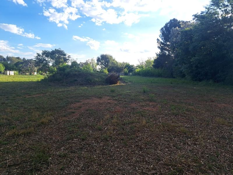 A view of a vacant residential plot featuring established trees and open grassy areas, suitable for future development.