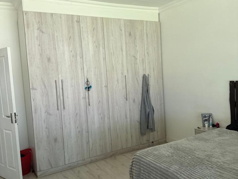 A well-maintained bedroom featuring light wood-look laminate flooring, neutral walls, and extensive floor-to-ceiling built-in cupboards with modern finishes.