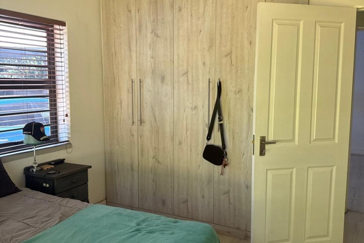 A bedroom featuring light wood-look built-in cupboards, laminate flooring, and a window with venetian blinds.