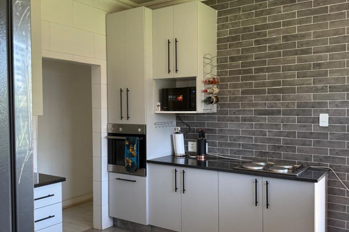 Modern kitchen featuring light cabinetry, dark stone countertops, a grey tiled feature wall, built-in oven, and hob, complemented by contemporary pendant lighting.