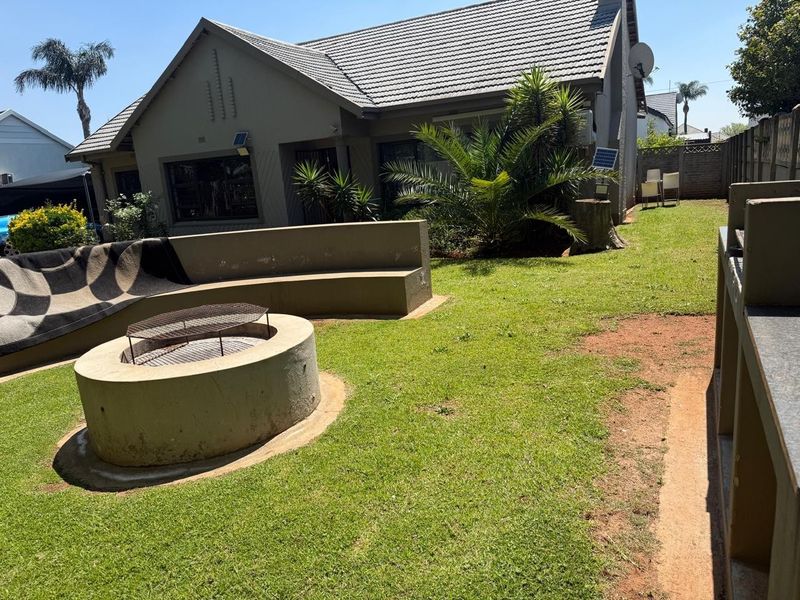 Rear garden area featuring a built-in fire pit, curved bench seating, and a fixed outdoor braai area, set against the rear elevation of the house.