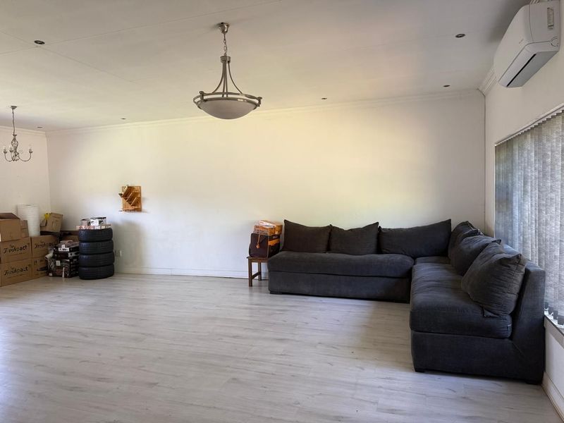 Spacious living room featuring light-toned laminate flooring, recessed downlighting, and a wall-mounted air conditioning unit.