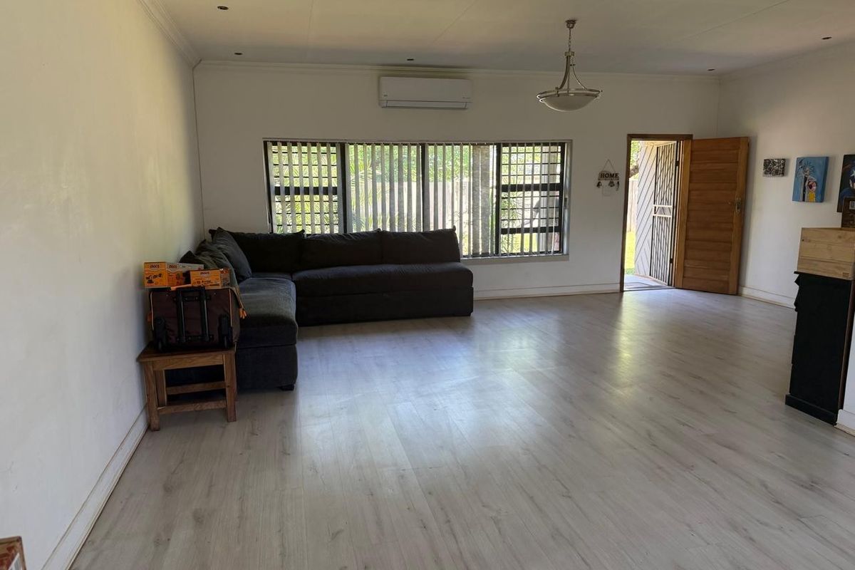 Spacious living area featuring light-toned laminate flooring, a wall-mounted air conditioning unit, and direct access to the exterior through a timber door.