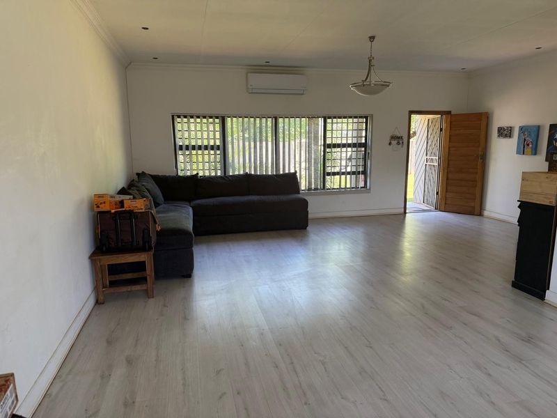 Spacious living area featuring light-toned laminate flooring, a wall-mounted air conditioning unit, and direct access to the exterior through a timber door.